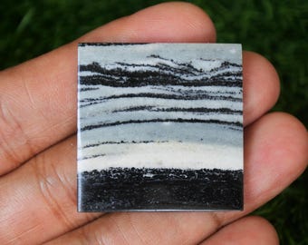 May include: A square, black and white banded agate cabochon with a white band in the center. The stone has a polished, smooth surface.