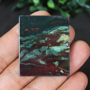 May include: A green, red, and white patterned stone cabochon. The stone has a layered, swirling pattern.