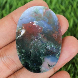 May include: Oval-shaped moss agate gemstone with a polished surface. The stone features a blend of colors, including deep green, red, blue, and white, creating a natural, artistic pattern. This gemstone is suitable for jewelry making.