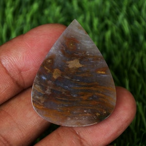 Peut inclure: Un cabochon d'agate en forme de larme avec des motifs bruns, blancs et dorés. La pierre est translucide et a une surface lisse et polie.