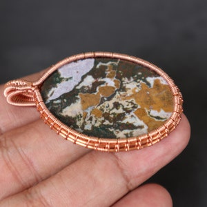 May include: A copper wire wrapped pendant featuring a brown, white and green agate stone.