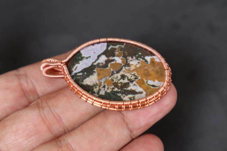 May include: A copper wire wrapped pendant featuring a brown, white and green agate stone.