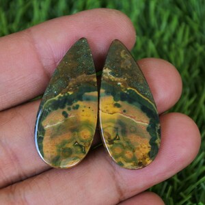 Peut inclure: Paire de cabochons en jaspe vert, jaune et brun en forme de larme. Les cabochons ont un motif marbré et sont polis pour une finition lisse.