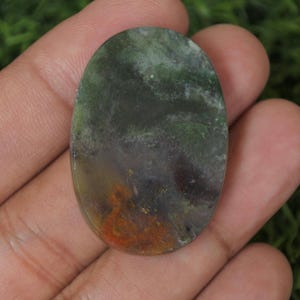 May include: Oval shaped green, brown, and white agate cabochon with a polished finish.