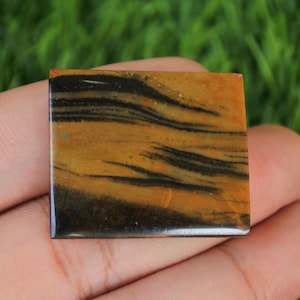 Könnte beinhalten: Ein quadratischer, polierter, gelber und schwarzer Edelstein mit einem gestreiften Muster.
