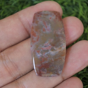 Può includere: Una pietra preziosa di agata tagliata a cabochon, lucidata, con un motivo di colore marrone, bianco e rosso. La pietra ha una forma rettangolare con bordi arrotondati.