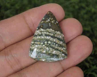 May include: A triangular gemstone with a distinctive pattern of green, brown, and white. The polished stone has a natural, organic appearance. The colours and patterns create a striking visual effect, suitable for jewellery or decorative purposes.