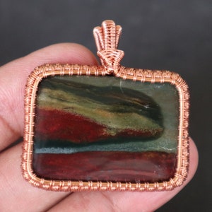 Peut inclure: Un pendentif en fil de cuivre enveloppé avec une pierre rectangulaire multicolore aux teintes rouges, vertes et brunes.
