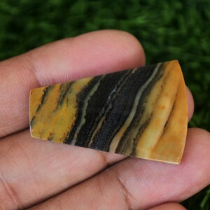 May include: A yellow and black banded agate cabochon with a triangular shape. The stone has a polished surface and is ready to be set in jewelry.