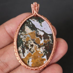Puede incluir: Pendiente envuelto en alambre de cobre con una piedra de ágata colorida con patrones marrones, blancos, verdes y amarillos.