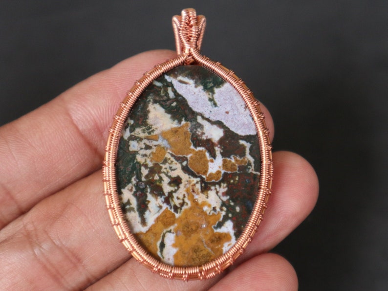 May include: Copper wire wrapped pendant featuring a colourful agate stone with brown, white, green, and yellow patterns.
