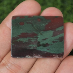 May include: A square, green, brown, and red jasper cabochon with a polished surface. The cabochon is approximately 2 inches wide and 1.5 inches tall.