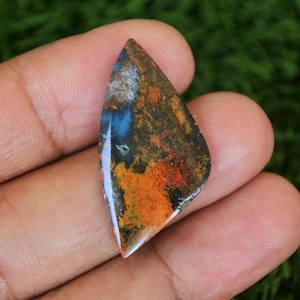 Op de afbeelding: Een kleurrijke, onregelmatig gevormde cabochon edelsteen met een mix van oranje, bruin, blauw en witte kleuren. De steen is gepolijst en heeft een glad oppervlak.