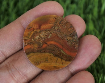 May include: A round, polished stone cabochon with a swirling pattern of brown, orange, and red colours. The stone has a natural, organic look.