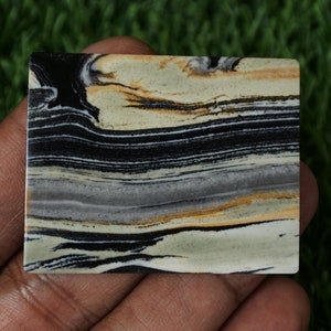 May include: A close-up of a polished slab of banded agate with black, white, grey, and brown stripes. The agate is smooth and has a natural, polished finish.