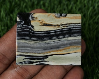 May include: A close-up of a polished slab of banded agate with black, white, gray, and brown stripes. The agate is smooth and has a natural, polished finish.