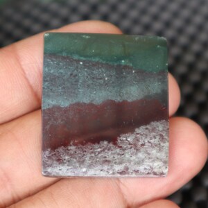 May include: A green, gray, and red banded agate cabochon with a white, cloudy pattern. The cabochon is rectangular and has a smooth, polished surface.