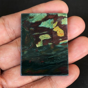 May include: A green, red, and yellow patterned stone cabochon with a smooth, polished surface.