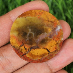 Op de afbeelding: Een ronde, gepolijste agaat cabochon met een mix van gele, oranje, rode en bruine kleuren. De steen heeft een uniek patroon van swirls en aderen.