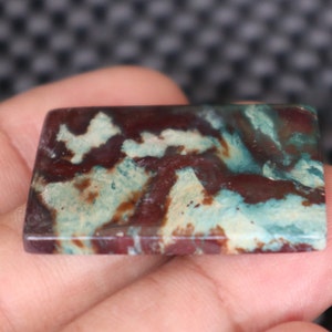 May include: A rectangular, polished, green, white, and brown agate cabochon with a swirling pattern.