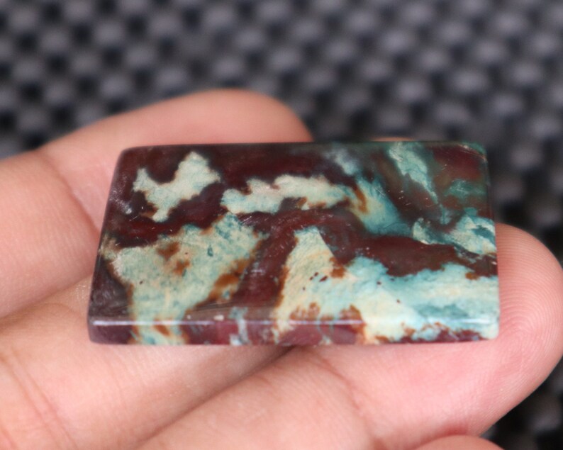 May include: A rectangular, polished, green, white, and brown agate cabochon with a swirling pattern.