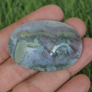 May include: A green, gray, and white agate cabochon with a swirling pattern. The cabochon is oval shaped and has a smooth, polished surface.