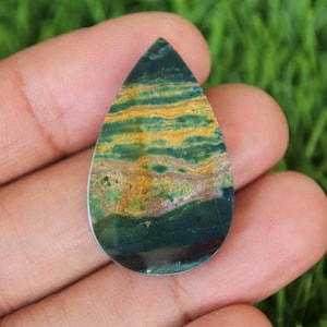 May include: A teardrop-shaped green, yellow, and brown gemstone cabochon with a polished finish.