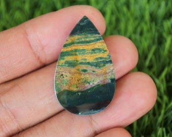 Könnte beinhalten: Ein tropfenförmiger grüner, gelber und brauner Edelstein-Cabochon mit polierter Oberfläche.