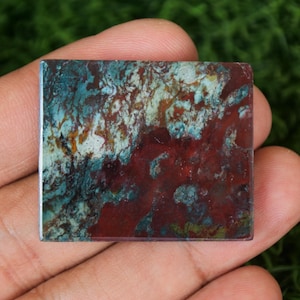 Może przedstawiać: Kwadratowy, czerwony, zielony i biały wzorzysty kamień kaboszonowy. Kamień ma marmurkowy, plamisty wygląd.