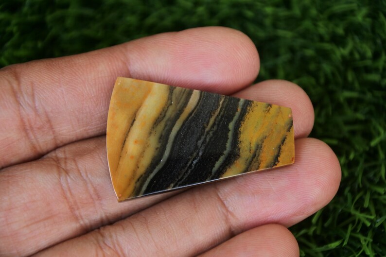 May include: A yellow, black, and white banded agate cabochon with a curved edge. The cabochon is approximately 2 inches long and 1 inch wide.