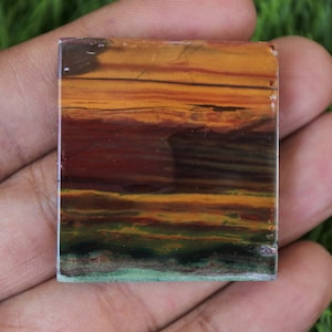 May include: A square piece of polished, multi-coloured agate with a layered pattern of red, orange, yellow, green, and black. The agate has a smooth, polished surface.
