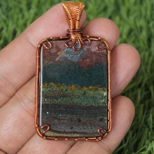 May include: A copper wire wrapped pendant featuring a rectangular, multi-coloured agate stone with shades of brown, green, red, and yellow.