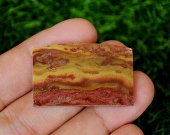 Könnte beinhalten: Nahaufnahme eines rot-gelb gebänderten Achat-Cabochons. Der Stein hat ein geschichtetes, gestreiftes Muster mit einer glatten, polierten Oberfläche.