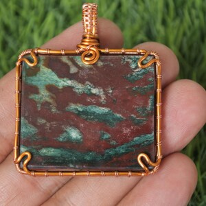 May include: A copper wire wrapped pendant featuring a square shaped red, green, and brown stone.