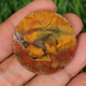 May include: A round, polished agate stone with a mix of yellow, orange, red, brown, and green colours. The stone has a natural, organic pattern.