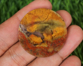 May include: A round, polished agate stone with a mix of yellow, orange, red, brown, and green colours. The stone has a natural, organic pattern.