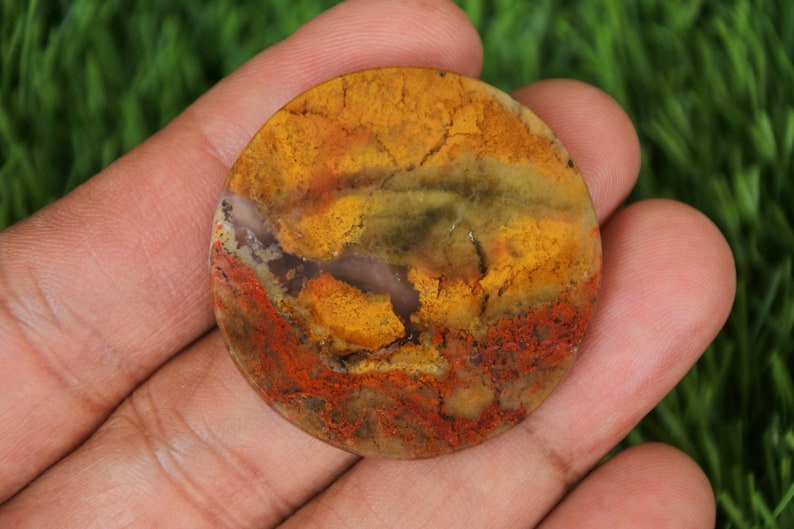 Op de afbeelding: Een ronde, gepolijste agaat steen met een mix van gele, oranje, rode, bruine en groene kleuren. De steen heeft een natuurlijk, organisch patroon.