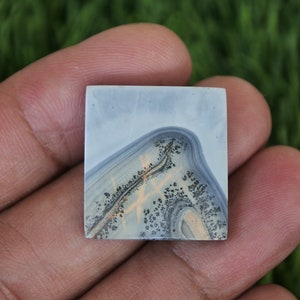 May include: A square, light blue agate cabochon with a white and black dendritic pattern. The agate has a smooth, polished surface.