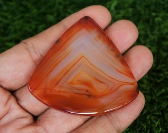 May include: A red agate gemstone with white and orange banding in a triangle shape.