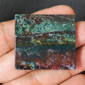 May include: A green, brown and red banded agate cabochon with a polished surface. The stone has a layered appearance with swirls of colour.