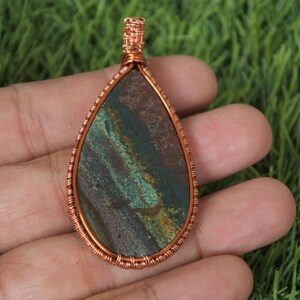 May include: A copper wire wrapped pendant featuring a teardrop-shaped stone with brown, green, and gold swirls.