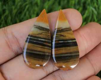 Könnte beinhalten: Zwei tropfenförmige, polierte, gebänderte Achat-Cabochons in einem braunen, schwarzen, weißen und orangefarbenen Farbschema.
