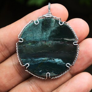 May include: A round green and black stone pendant with silver wire wrapped around the edge.