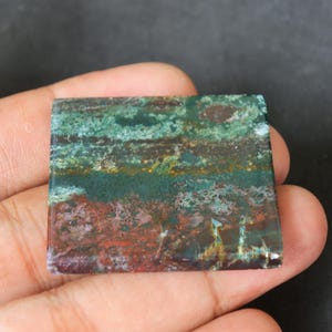 May include: A square, green, brown, and white patterned stone cabochon. The stone has a layered, banded appearance with a variety of colours and textures.