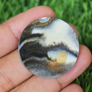 May include: A round, white, black, and gold agate cabochon with a swirling pattern. The cabochon is about 2 inches in diameter.