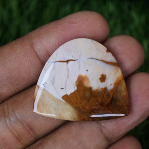 Könnte beinhalten: Ein weißer und brauner Achat-Cabochon in Tropfenform. Der Stein hat ein einzigartiges Muster aus weißen und braunen Wirbeln.