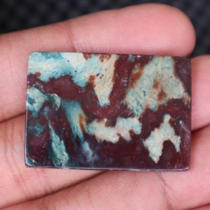 May include: A rectangular, polished, green, brown, and white agate cabochon with a swirling pattern.