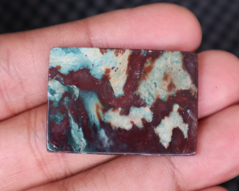 May include: A rectangular, polished, green, brown, and white agate cabochon with a swirling pattern.