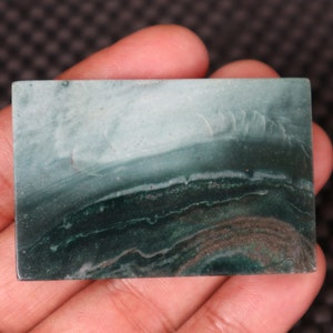 May include: A green and white banded agate cabochon with a smooth, polished surface. The stone has a layered appearance with shades of green and white.