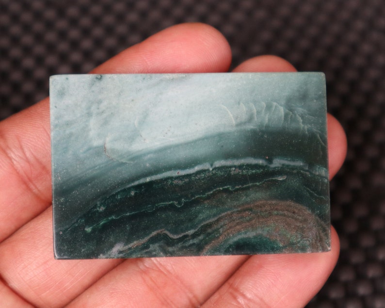 May include: A green and white banded agate cabochon with a smooth, polished surface. The stone has a layered appearance with shades of green and white.